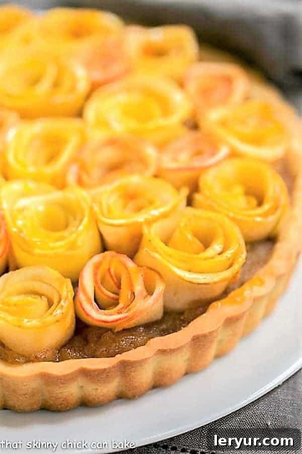 Close-up view of a Rosette Apple Tart, highlighting the detailed texture of the apple roses and the rich applesauce filling, served on a white cake plate.