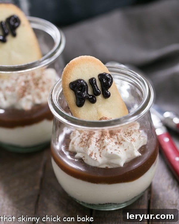 Midnight Graveyard Parfaits 3 Close-up view of a Fudgy Tombstone Parfait, beautifully layered with chocolate cookie crumbs, creamy no-bake cheesecake, and rich fudge, topped with a Milano cookie inscribed with 'RIP'.