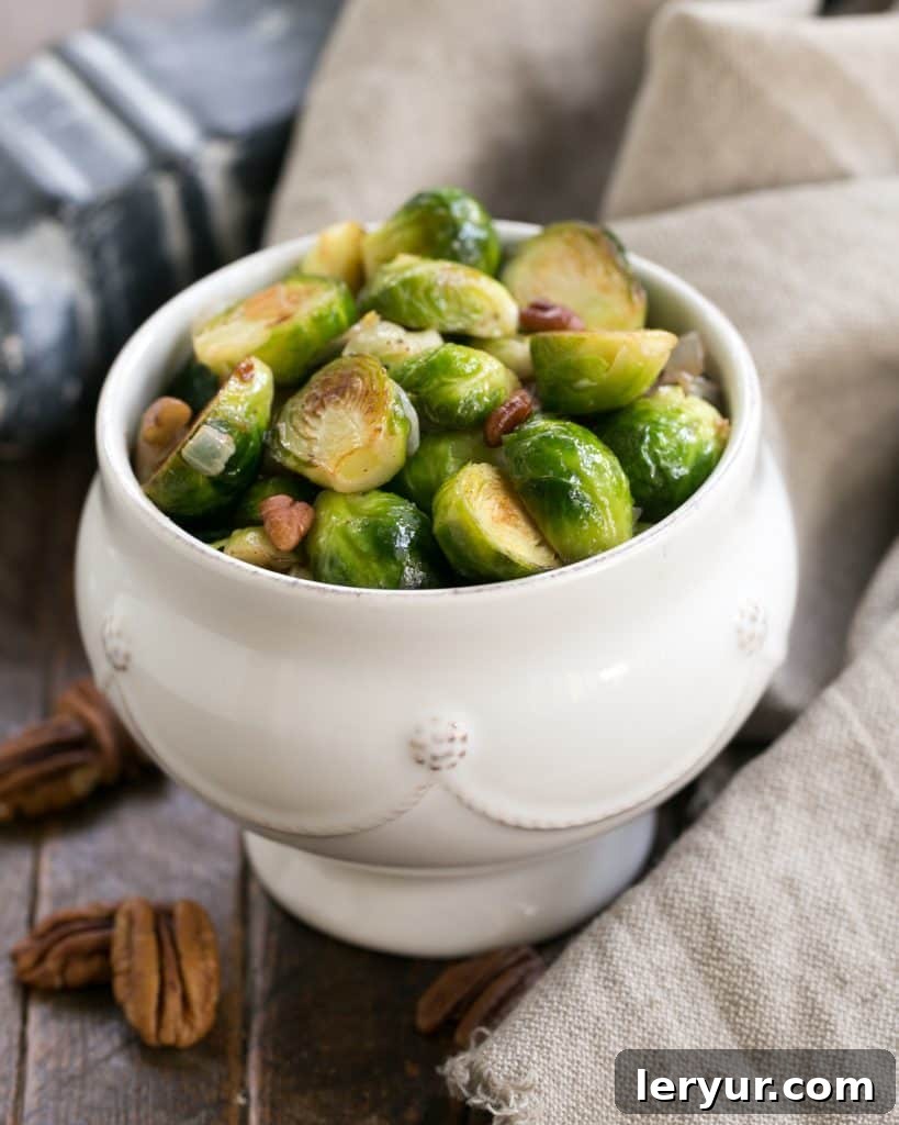 A white bowl of golden-brown sautéed Brussels sprouts, garnished with chopped pecans.