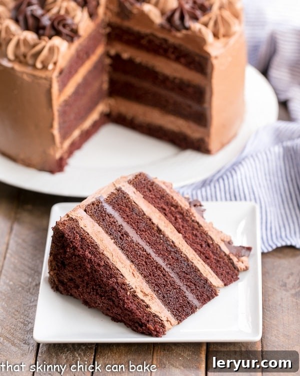 A stunning Chocolate Fudge Layer Cake with a perfect slice resting on a square white plate, revealing its many layers of moist cake, silky ganache, and fluffy buttercream. The main cake stands majestically in the background.