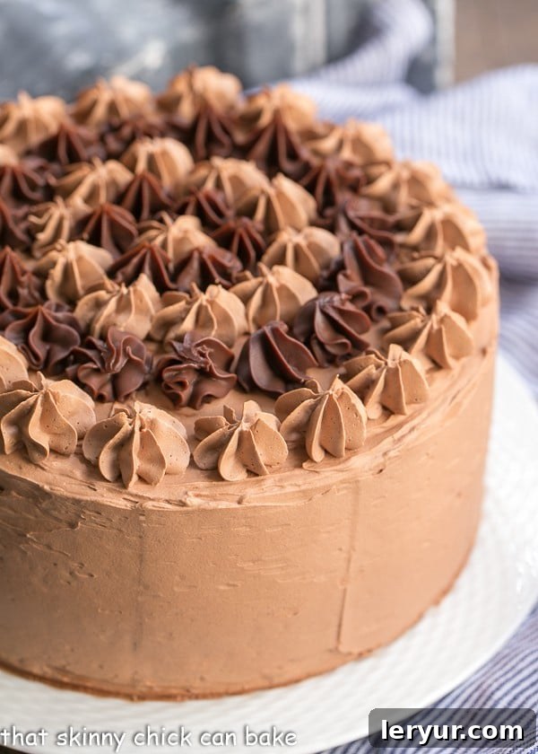 A magnificent, uncut Chocolate Fudge Layer Cake, perfectly frosted and ready to be sliced, sitting proudly on a pristine white cake stand.