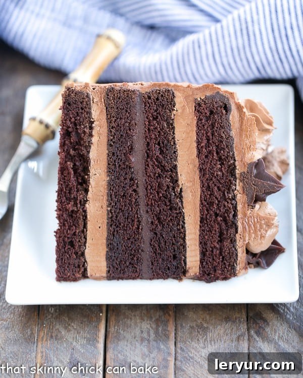 A delectable slice of Chocolate Fudge Layer Cake, beautifully showcasing its layers of moist cake, rich ganache, and fluffy buttercream, resting invitingly on a white square plate.