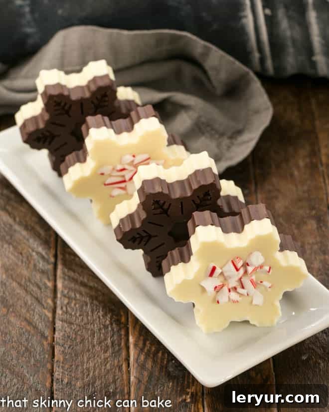 Peppermint Bark Snowflakes, beautifully layered with dark and white chocolate, and adorned with vibrant candy cane shards, neatly lined up on a narrow white tray, highlighting their crisp presentation.