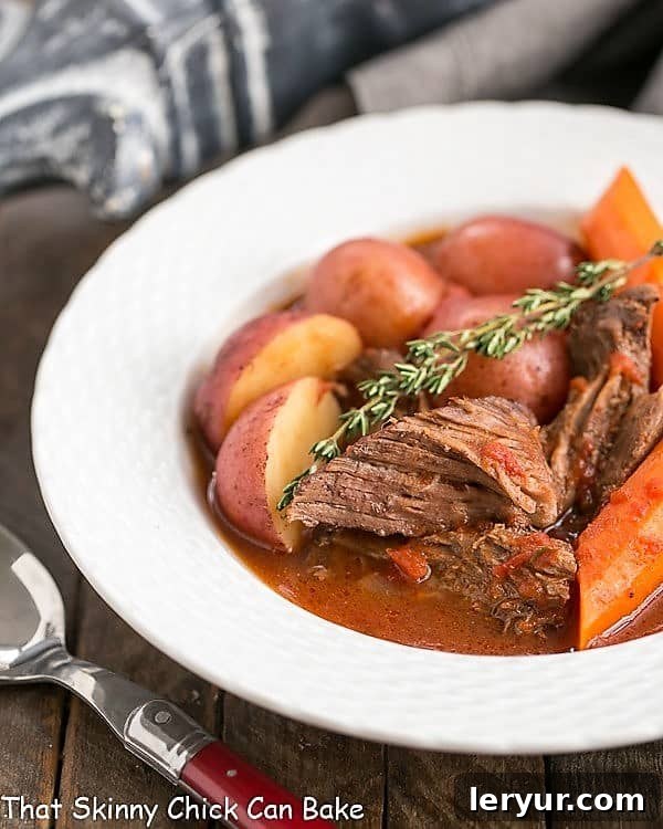 Easy Pot Roast - Slow cooked comfort food with beef, wine, tomatoes, carrots and potatoes Easy Pot Roast in a shallow white bowl with a sprig of thyme.