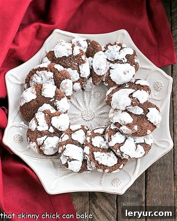 Chocolate Crinkle Cookies - Fudgy cookies dusted in powdered sugar! A ring of Chocolate Crackle Cookies on a white serving plate.