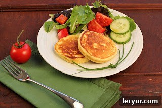 A stack of perfectly fried Matafan potato pancakes resting on a white plate, accompanied by a neatly folded green napkin, highlighting their inviting texture