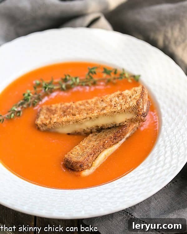 Homemade Tomato Soup with Thyme - A luscious classic made without cream and served with grilled cheese fingers! Thyme Kissed Tomato Soup in a white bowl with grilled cheese and thyme, highlighting its creamy texture.
