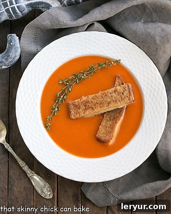 Homemade Tomato Soup - A luscious classic made without cream and served with grilled cheese fingers! Thyme Kissed Tomato Soup in a white bowl overhead view, showcasing its smooth texture and fresh thyme garnish.