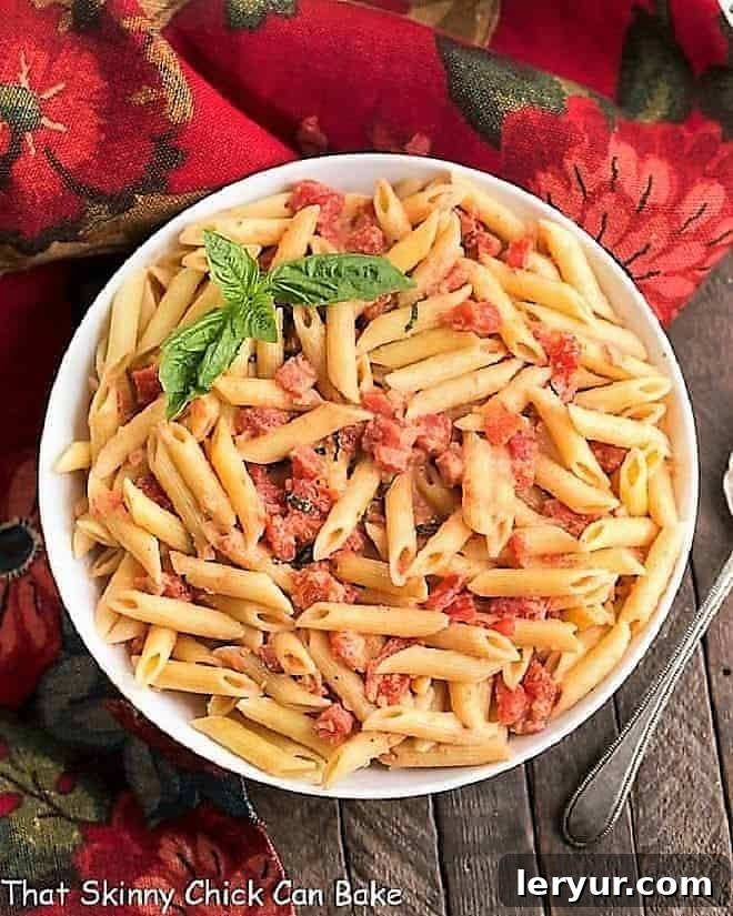 A top-down view of Penne alla Vodka served in a white serving bowl, garnished with fresh basil leaves.