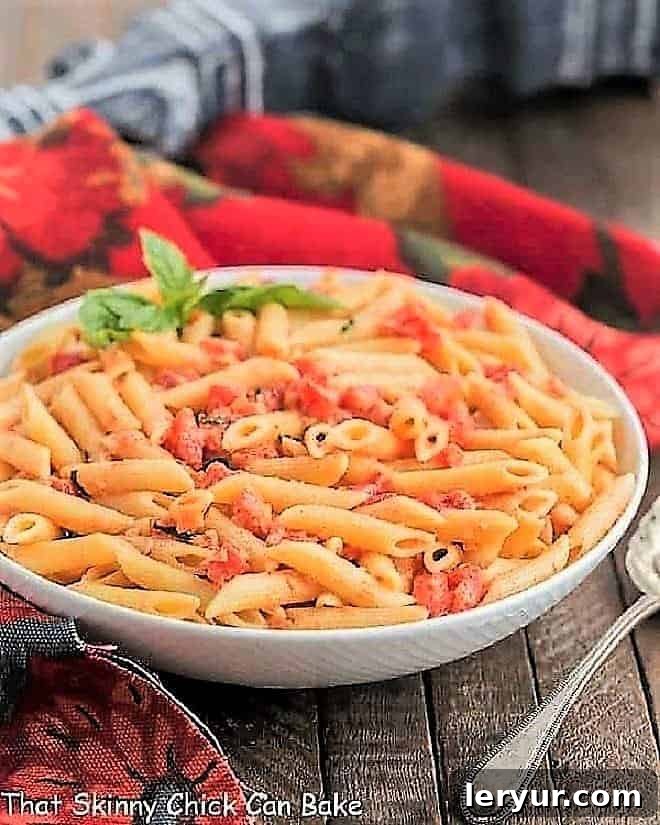 Penne alla Vodka in a white ceramic bowl, garnished with a sprig of fresh basil, ready to be enjoyed.