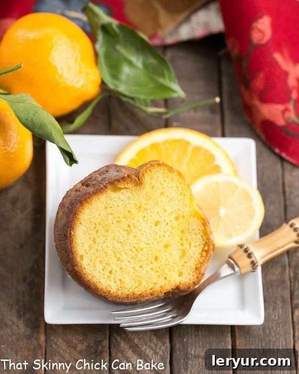 A beautifully sliced Easy Lemon Bundt Cake on a square white plate, elegantly garnished with fresh lemon and orange slices, highlighting its moist crumb.