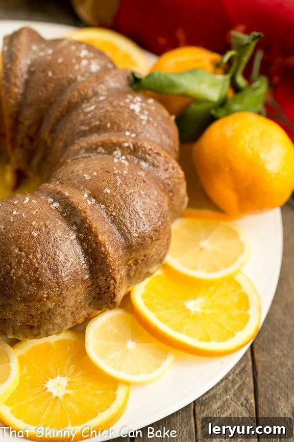 A glorious Easy Lemon Bundt Cake displayed on a white cake plate, adorned with vibrant lemon and orange slices, ready to be served.