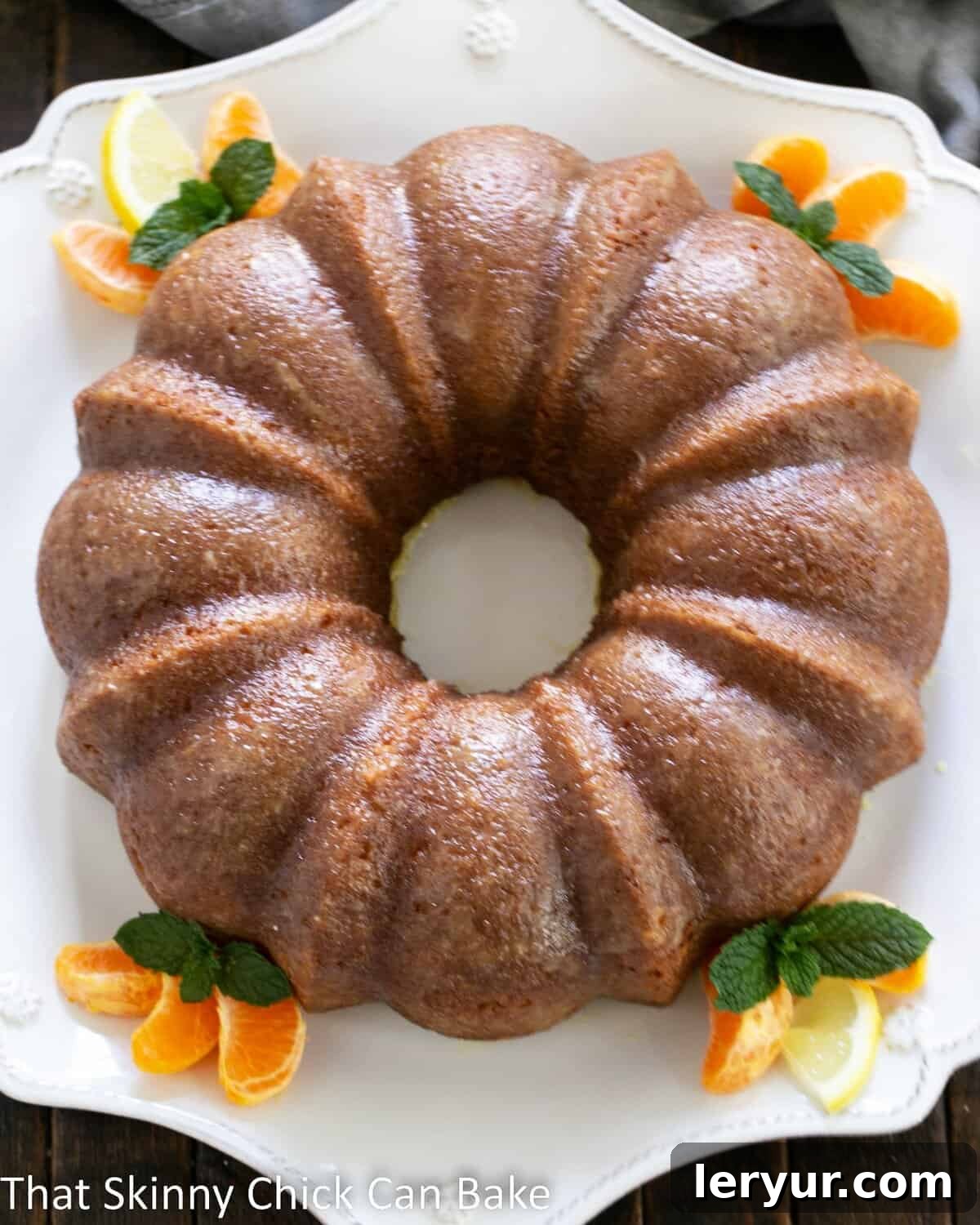 Overhead shot of the full Easy Lemon Bundt Cake on a clean white cake plate, showing off its beautiful form and golden glaze.