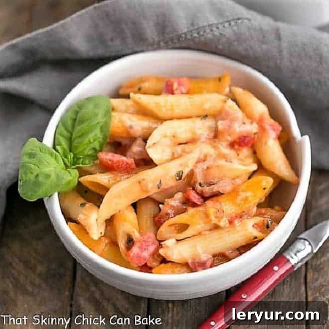 Overhead view of Cheesy Baked Pasta in a white bowl with a sprig of basil