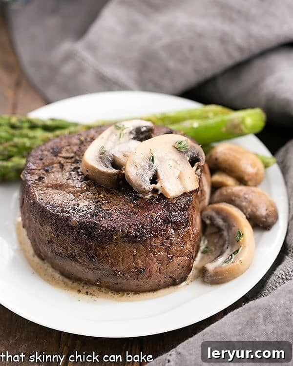 Mushroom Topped Pepper Steak topped with mushrooms on a white plate with asparagus spears
