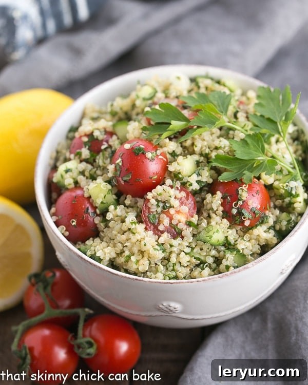 A beautifully presented white bowl of Quinoa Tabbouleh, garnished with fresh parsley and mint, showcasing its vibrant green and red hues.
