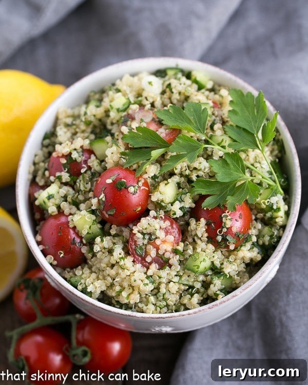 Overhead shot of a large white bowl filled with a vibrant Quinoa Tabbouleh, featuring finely chopped parsley, mint, tomatoes, and cucumber mixed with fluffy quinoa.