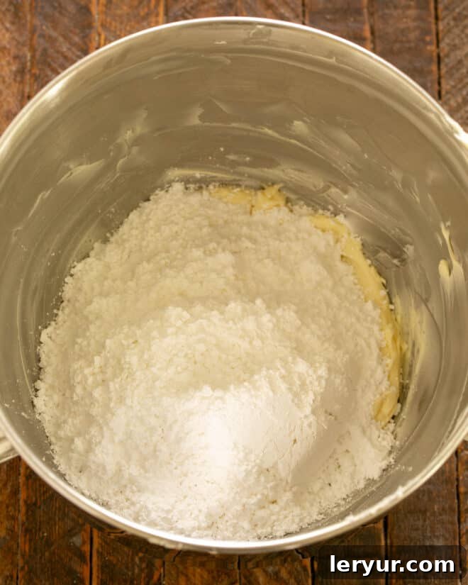 Beating room temperature butter with sifted powdered sugar in a large bowl to create the base for the chocolate frosting.