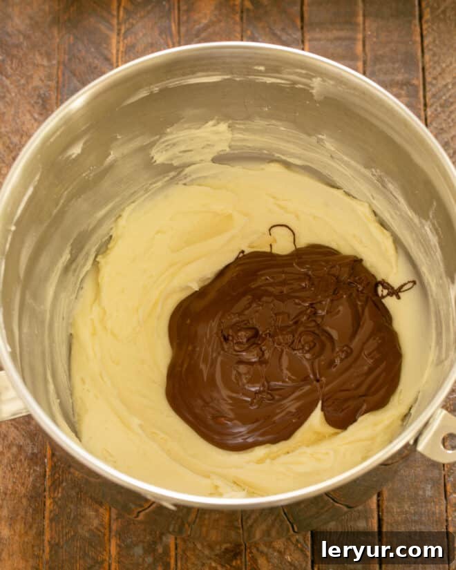Adding cooled melted chocolate and vanilla extract to the butter and powdered sugar mixture for the frosting.