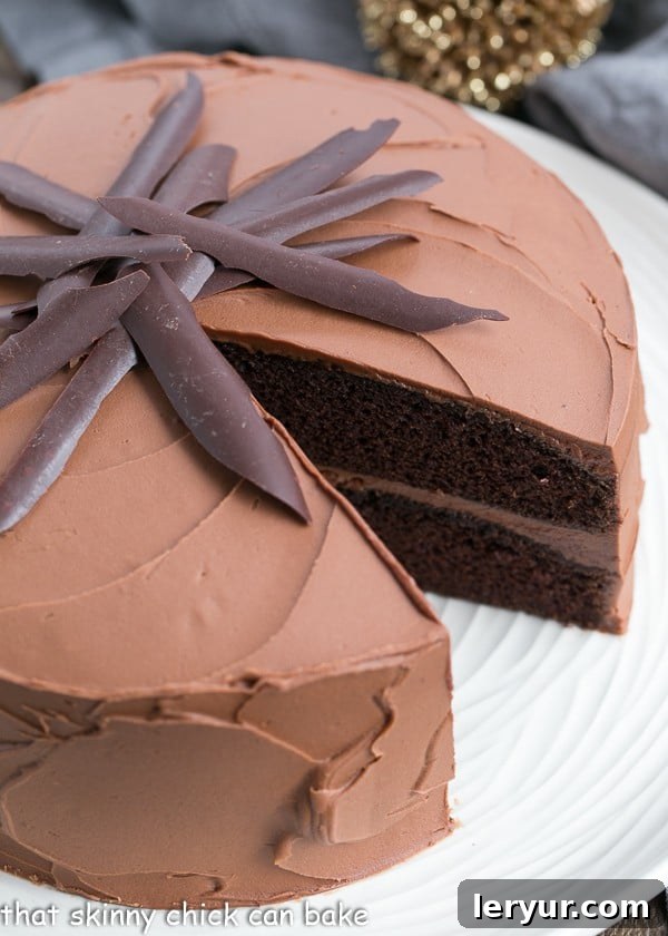 A beautifully decorated Chocolate Mayonnaise Cake with a single slice removed, revealing its moist interior, placed on a white serving plate.