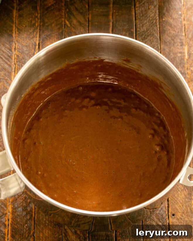Scraping down the sides of the mixing bowl with a spatula to ensure all ingredients are fully incorporated into the chocolate cake batter.