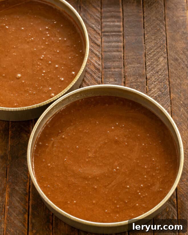 Dividing the prepared chocolate mayonnaise cake batter evenly into two greased and parchment-lined round cake pans.