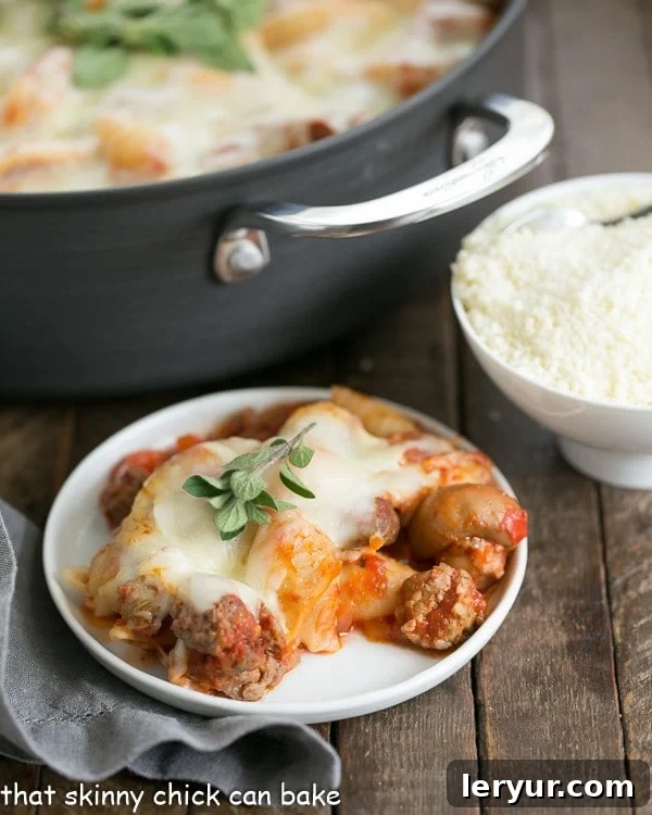 A white dinner plate piled high with Cavatini Supreme, with a large casserole pan full of the dish in the background.