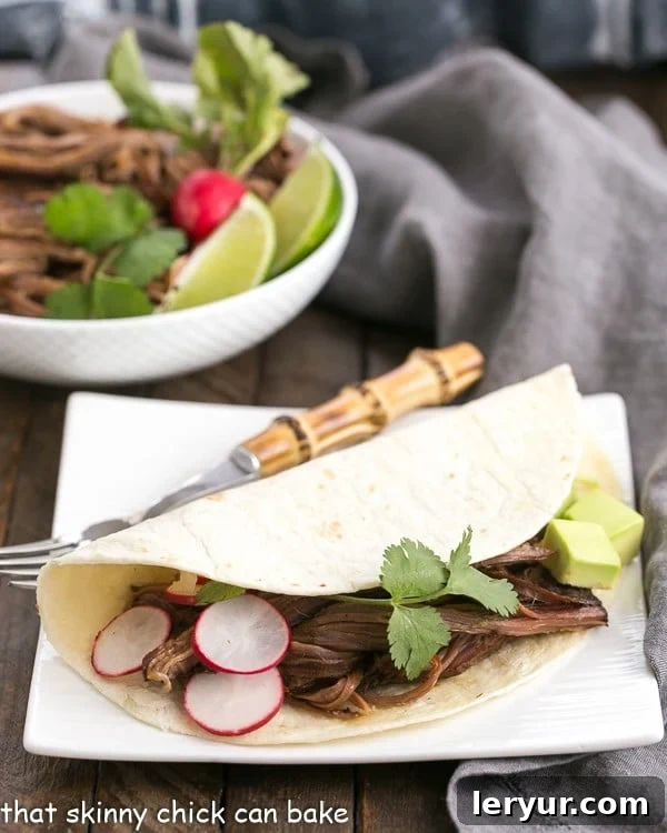 Slow Cooker Carne Asada - The classic Latin dish made in a slow cooker for ultimate tenderness! Slow Cooker Carne Asada in a tortilla on a square white plate, garnished with fresh cilantro and lime wedges.