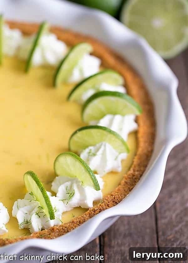Close-up view of a whole Key Lime Pie, showcasing its smooth, light green filling and crumbly graham cracker crust, in a white ceramic pie plate.