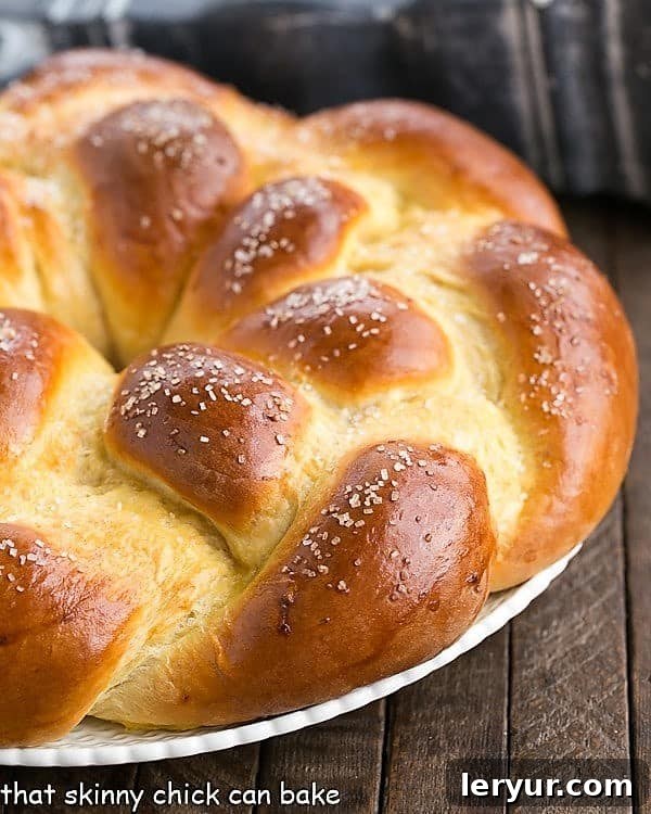 A beautifully golden-brown, braided loaf of Easter bread resting on a white ceramic platter, ready to be sliced and served.