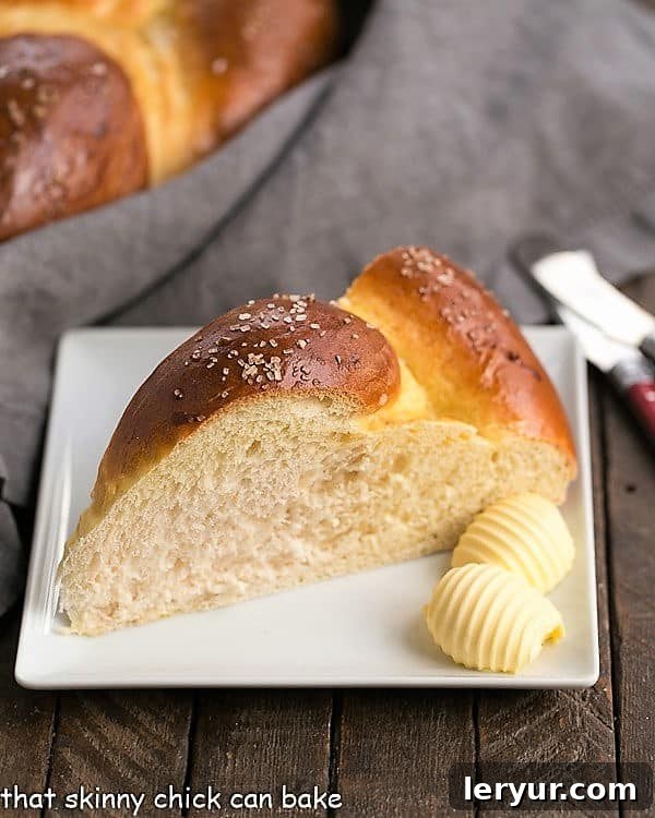 A single, perfectly golden-brown slice of Braided Easter Bread rests on a square white plate, accompanied by two melting pats of butter.