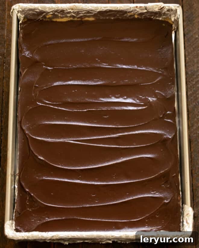 Irresistible Peanut Butter Truffle Brownies 12 Chocolate ganache being spread over the peanut butter layer of the brownies.