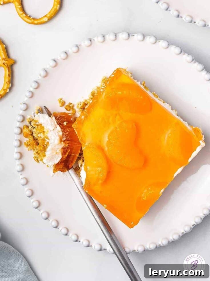 A vibrant mandarin orange jello pretzel salad with layers.
