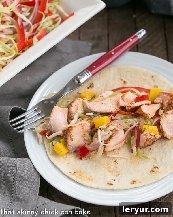 Fish Tacos Recipe with Salmon and Mango Salsa - Roasted salmon with all the fixings for a sophisticated seafood taco Fish Tacos Recipe with Salmon and Mango Salsa on a round white plate with a red handled fork. Perfectly roasted salmon tacos for a healthy and delicious meal.