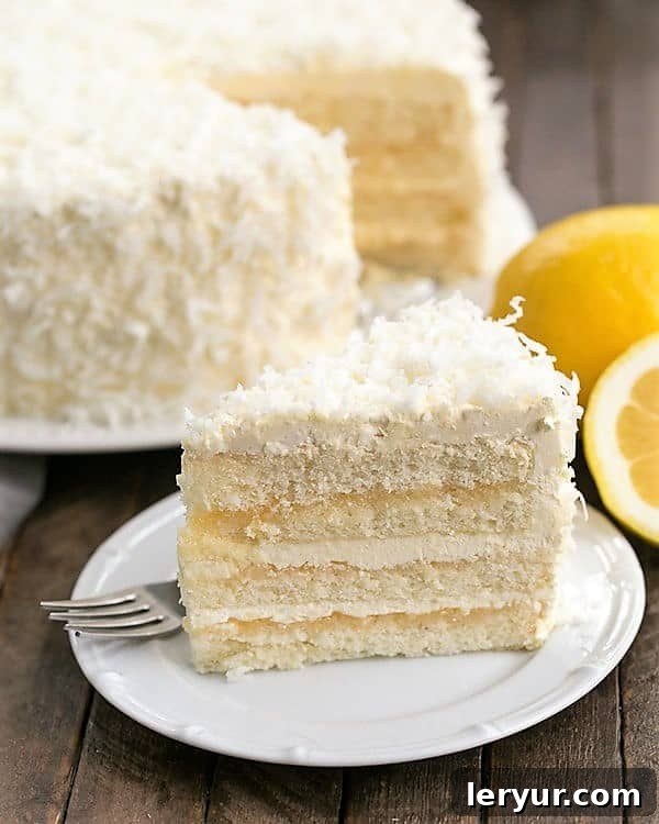 A beautifully sliced Lemon Layer Cake revealing vibrant yellow lemon curd and fluffy white Swiss Meringue Buttercream layers on an elegant white dessert plate, ready to be enjoyed.