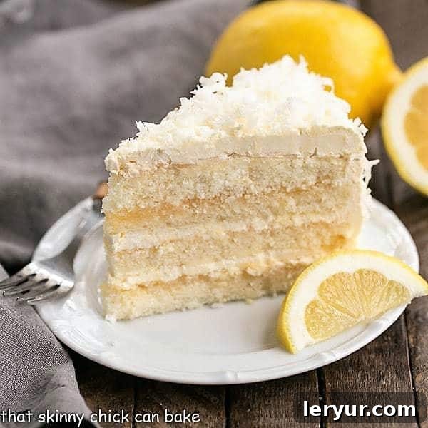 A close-up of a perfectly cut slice of Lemon Layer Cake, showcasing distinct layers of bright yellow lemon cake, tangy lemon curd, and fluffy white Swiss Meringue Buttercream, elegantly garnished with a fresh lemon wedge on a white ceramic plate.