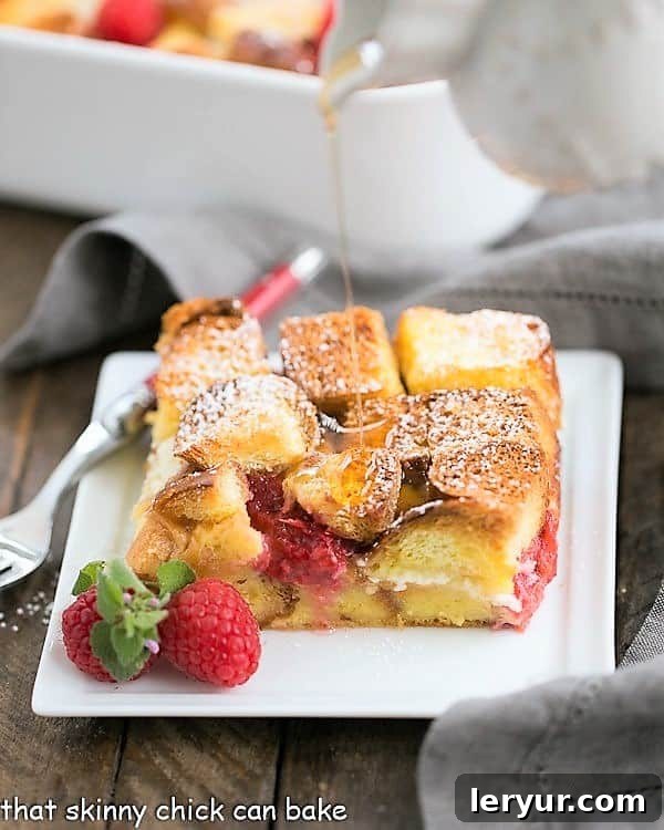 Raspberry Mascarpone French Toast Casserole on a white plate with a drizzle of maple syrup.