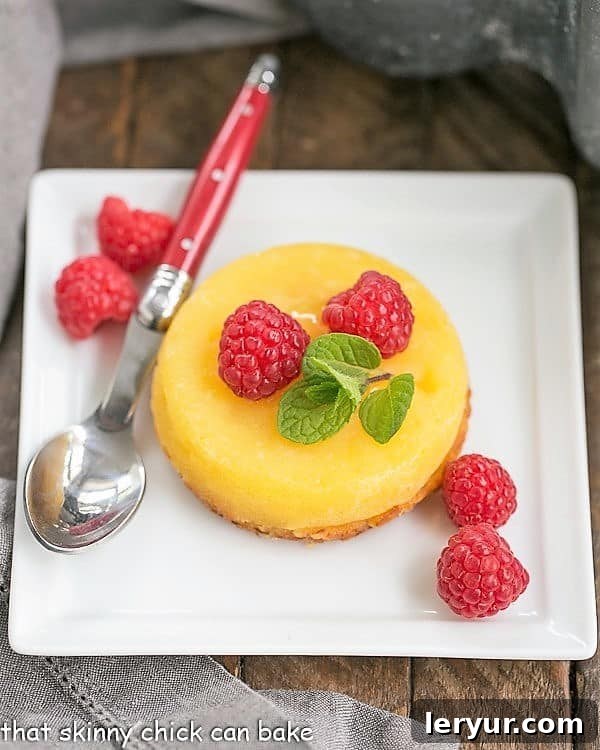 White Chocolate Molten Lava Cakes - Dreamy individual white chocolate cakes with molten centers! Two exquisite White Chocolate Molten Lava Cakes presented on a square ceramic plate, garnished with fresh, vibrant raspberries for a touch of color and tartness.