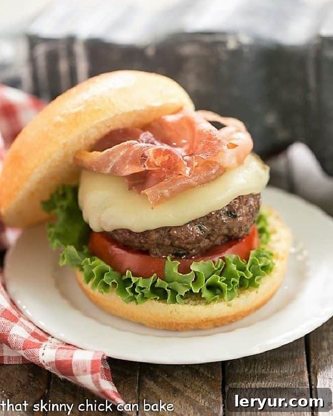 Irresistible Italian Pesto Burger - Pesto-infused patties topped with gooey mozzarella and crispy prosciutto for the ultimate gourmet experience! Italian Pesto Burger topped with cheese and prosciutto on a small white plate