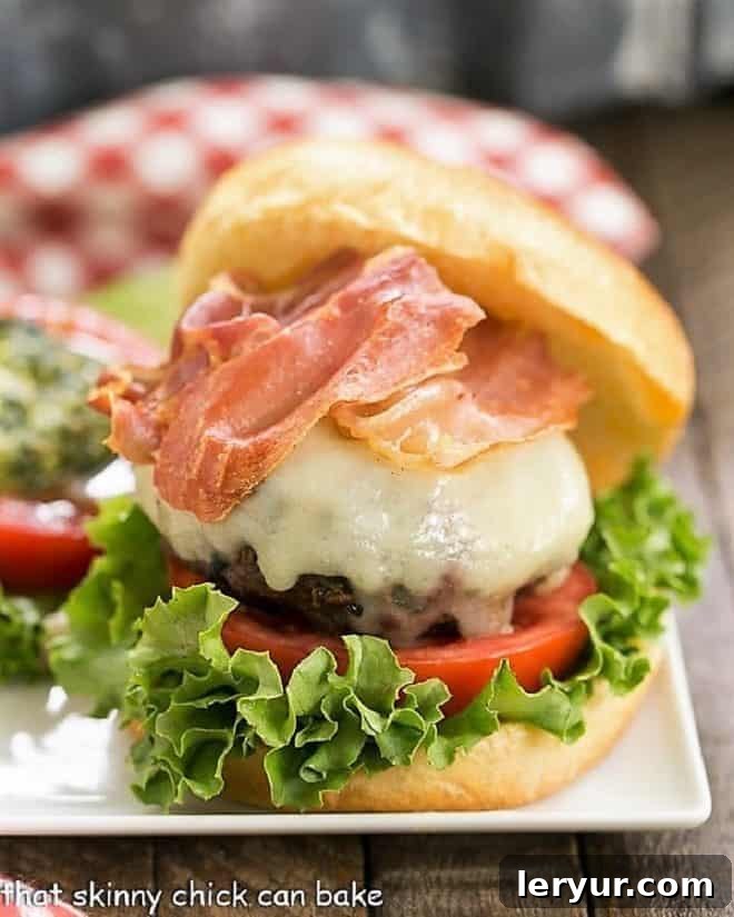 Perfectly Grilled Italian Burger - Pesto-spiked patties crowned with melted mozzarella and crunchy prosciutto! A delicious and gourmet way to transform your burger night. Close up view of Italian Pesto Burger with toppings on a square plate