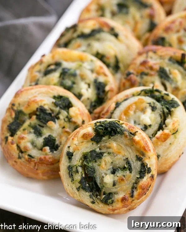 Spinach Feta Pinwheels - The marvelous flavors of Greek spanakopita without all the work! Golden brown, flaky Spinach Feta Pinwheels arranged beautifully on a white serving tray, ready to be enjoyed.