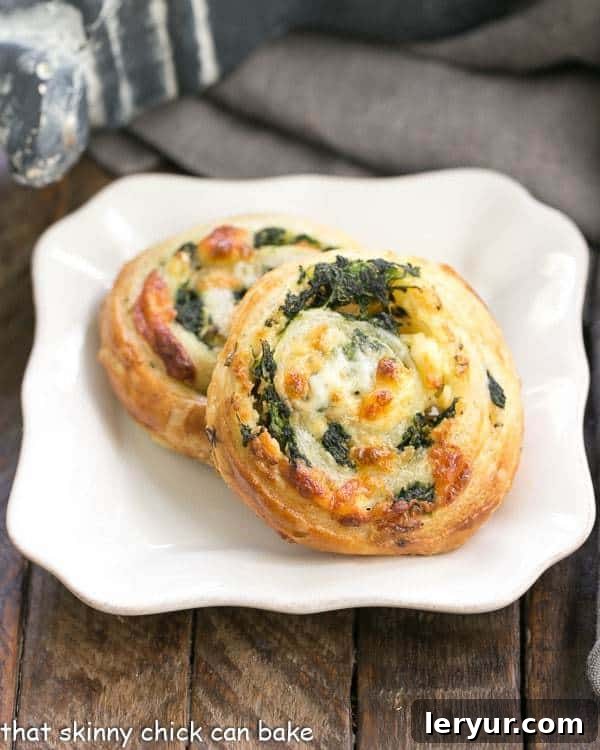 Spinach Feta Pinwheels -The marvelous flavors of Greek spanakopita without all the work! A cluster of freshly baked Spinach Feta Pinwheels on a white square plate, showcasing their golden crust and visible filling.