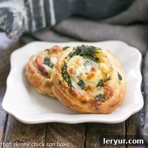 Two spinach feta pinwheels on a white plate, showcasing their golden, flaky crust and savory filling.