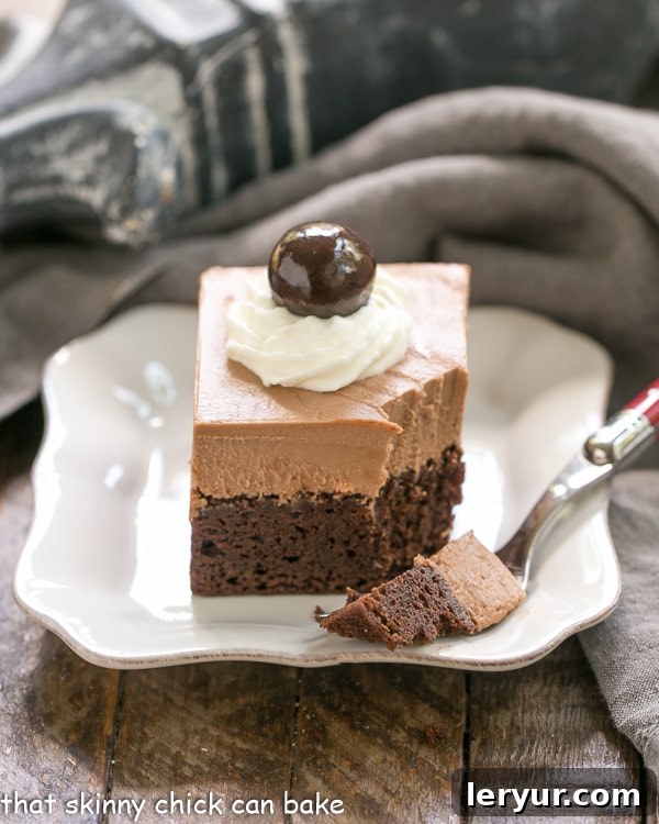 French Silk Pie Brownies - A spectacular 2-in-1 dessert that's a cinch to prepare! A square French Silk Pie Brownie with a portion removed, resting on a white square plate, highlighting the creamy filling.