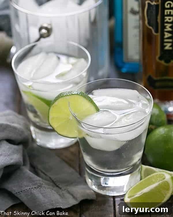 Two St. Germain Gin and Tonic Cocktails in elegant glasses, garnished with fresh lime wedges, sitting on a rustic wooden surface with a soft, inviting backdrop.