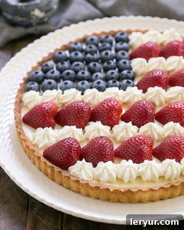 American Flag Fruit Tart - Pate sablee crust, light cream cheese filling and berries and cream stars and stripes! American Flag Fruit Tart on a white ceramic plate, showcasing its vibrant berry decoration.