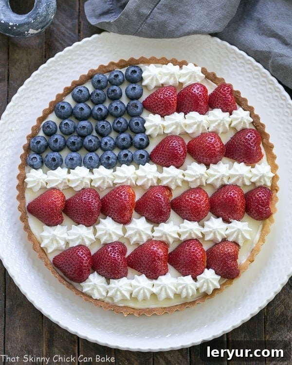 American Flag Fruit Tart - Pate sablee crust, light cream cheese filling and berries and cream stars and stripes! Overhead view of an American Flag Fruit Tart on white serving plate, highlighting the detailed berry arrangement.