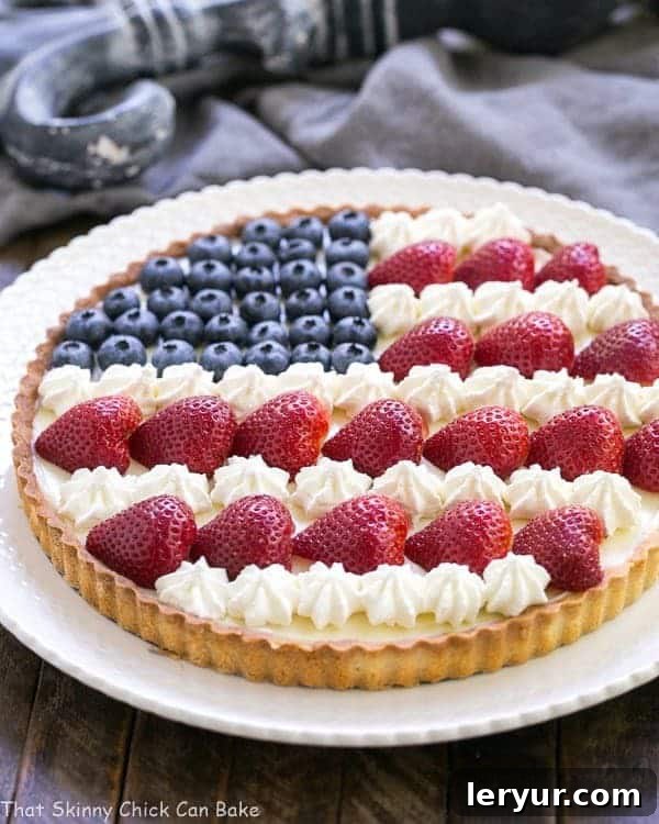 American Flag Fruit Tart - Pate sablee crust, light cream cheese filling and berries and cream stars and stripes! American Flag Fruit Tart on a white serving plate, ready to be enjoyed.