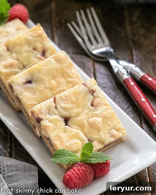 Decadent White Chocolate Raspberry Delight 2 White chocolate raspberry bars on a white tray with raspberries and mint.