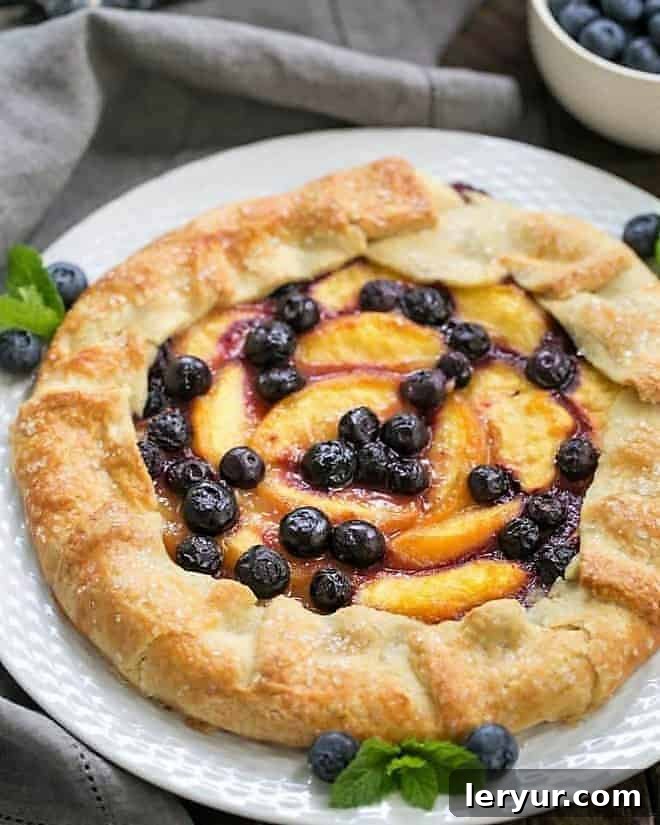 Peach Blueberry Galette - A gorgeous summer dessert with all the flavors of pie without all the work! A stunning Peach Blueberry Galette, perfectly baked with a golden crust and glistening fruit filling, displayed on a pristine white serving plate.